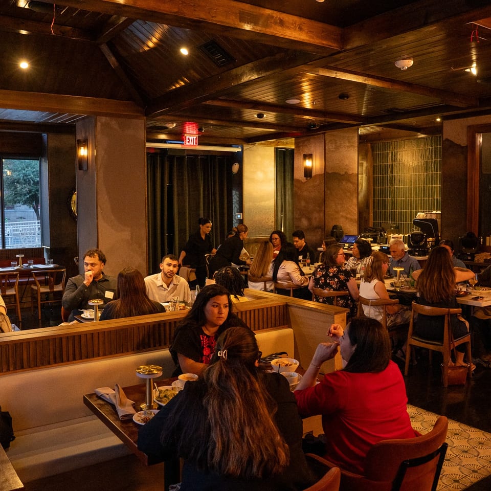 Busy restaurant interior with many patrons dining at tables and booths under warm lighting.