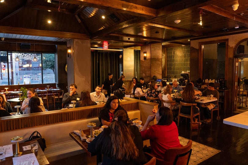 Busy restaurant interior with many patrons dining at tables and booths under warm lighting.